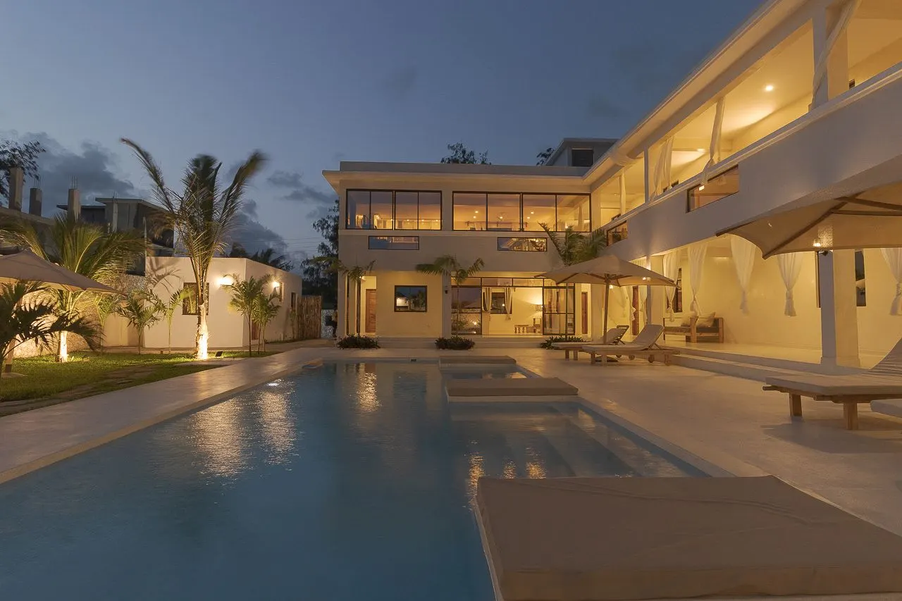 The TAWI courtyard pool lit up at dusk, with palms and the two-storey guest wing behind